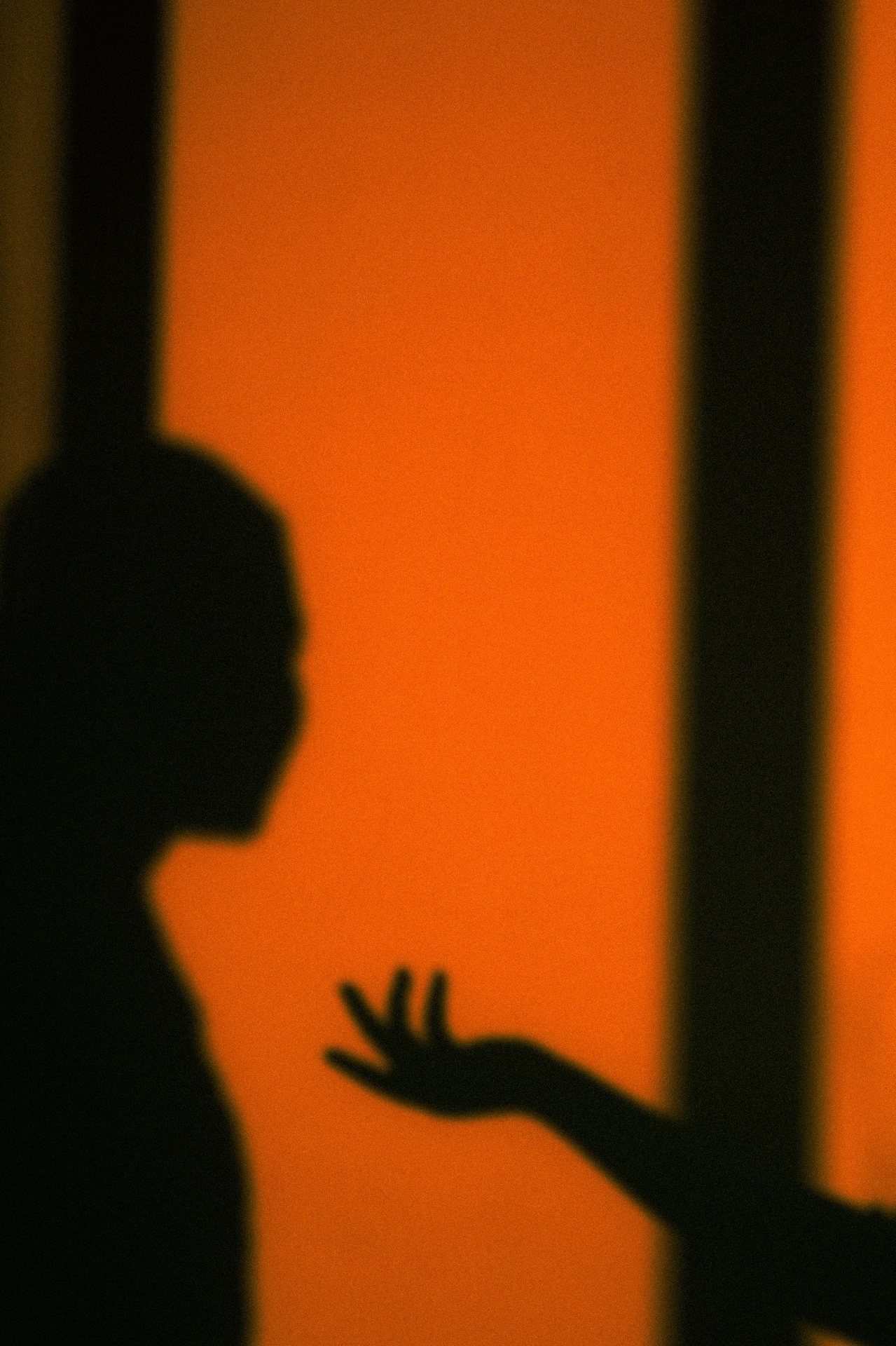 Silhouette of a child reaching out a hand against an orange wall