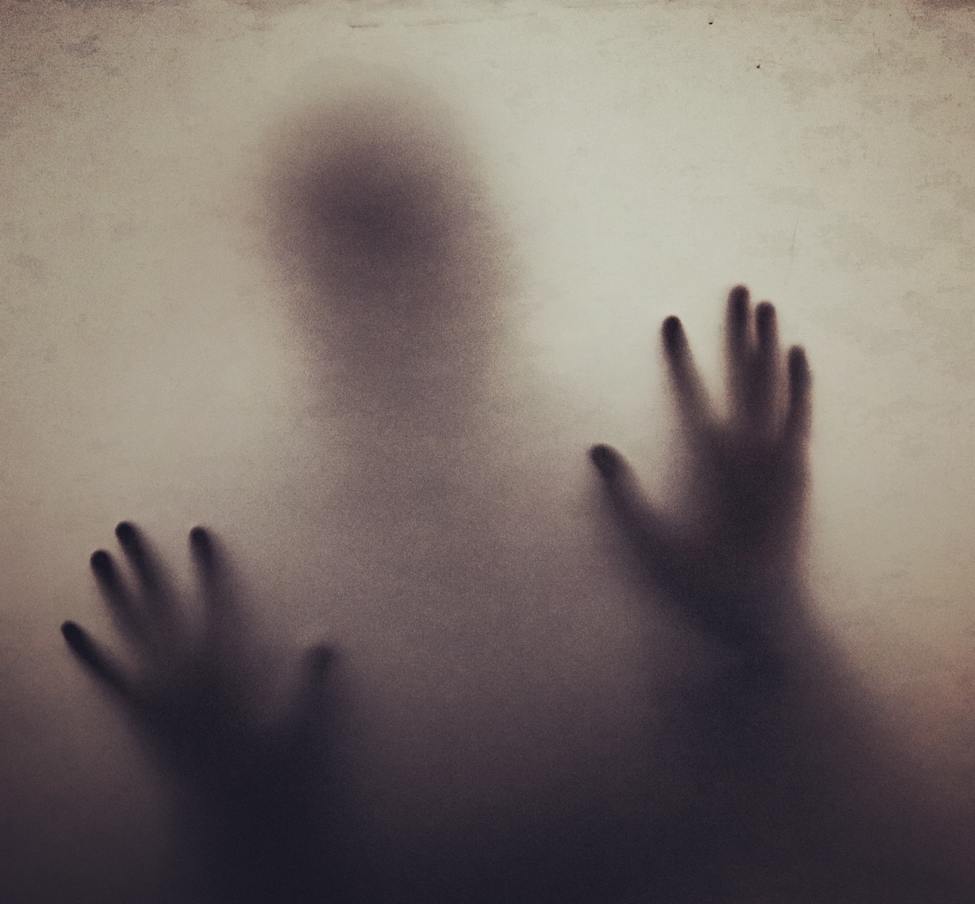 Silhouette of a person with hands pressed against frosted glass